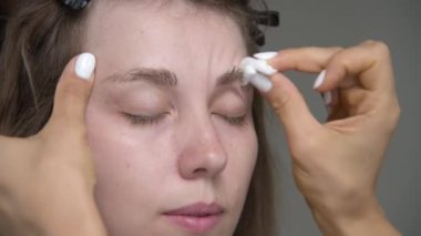 Güzellik uzmanı müşterilerin kaşlarını temizliyor. Kaşları kalıcı renge hazırlıyorum. Kafkasyalı genç bir kadının yüzüne ve bir kozmetikçinin ellerine yakından bakın.