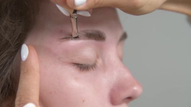 Güzellik salonunda kadın kaşlarının kalıcı renklendirilmesi için profesyonel prosedürler. Kaş boyama. Müşterilerin yüzlerini ve çalışan stilistleri yakından çek. 4K biçiminde sinematik görüntüler