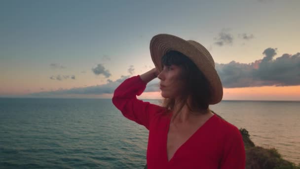 여자의 클로즈업 초상화 그녀의 바람에 바다에서 일몰을 모자와 우아한 드레스에있는 — 비디오