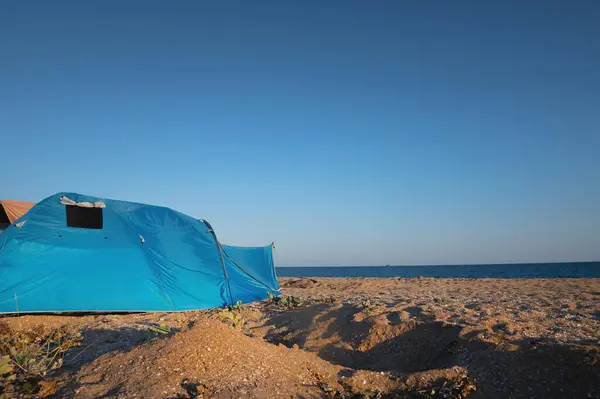 Tent, summer camping on the beach, against the backdrop of the sea and sky. A bright blue large tent stands on the sandy shore, no one.