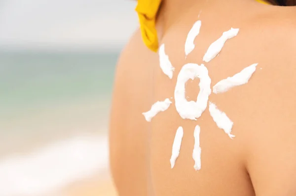 woman with sun-shaped suntan lotion on her shoulder, relaxing on the beach and taking care of her health. happy girl with the sun on her back by the sea in nature.