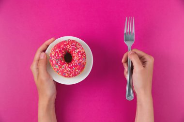 Kadın eli tabakta donut, pembe arka planda çatal tutuyor. Üst manzara, düz yatış. Güzel, diyet konsepti. Tatilden sonra kilo vermek..