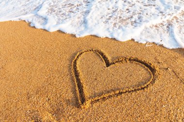Gün batımında kumsalda kalp çizilmiş. Kalp şeklinde. Kalp sembolü. Sevgi. Deniz köpüğü..