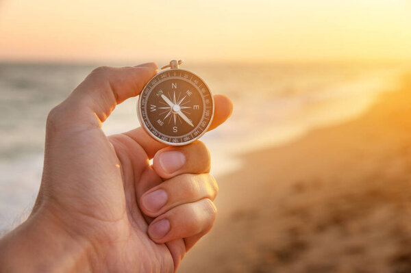 a mans hand holds a compass on the beach. Hand with compass over sand by the sea, direction and adventure concept