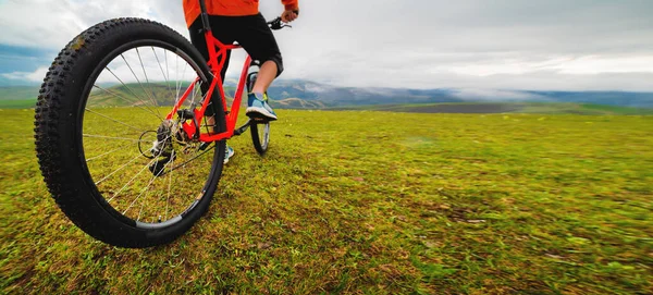 stock image Panoramic shot of a cyclist on a mountain bike against a background of green hills and mountains in the clouds. Mountain bike banner.