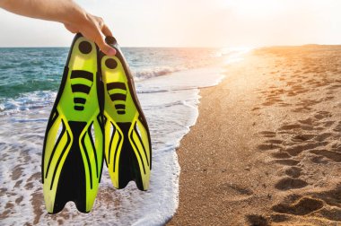 Bir adam deniz kıyısının arka planına karşı yüzgeçlerini elinde tutar. Şnorkelle yüzmek için vahşi doğada yaz tatili