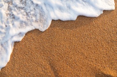 Deniz kıyısına bir dalga vuruyor. Yakın plan beyaz köpük altın kumlu kumda uzanıyor.