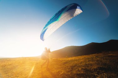 Yerin üstünde bir paraglider uçmaya hazırlanıyor. Profesyonel bir atlet, güneşli bir günde paraşütünü sarı bir tarlaya kaldırdı.