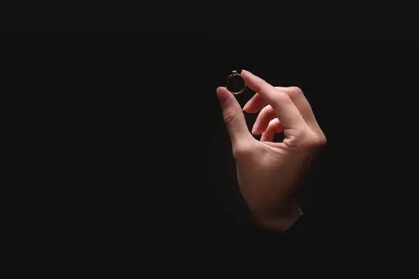 Close-up of a womans hands with an elegant diamond ring on a black background. A diamond ring is given out of the darkness by a womans hand.