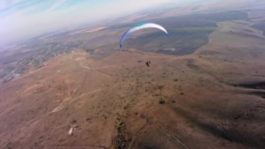 Paraşütçü bir sporcu, güneşli bir sonbahar gününde bir köyün yakınındaki küçük bir dağın yamacında yamaç paraşütü üzerinde uçar. FPV İHA kuadkopteri ile akro modda hava görüntüleme çekimi.