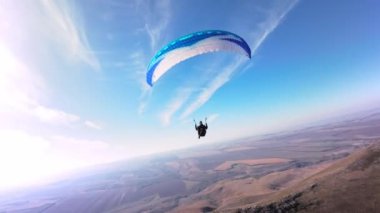 Paraşütçü bir sporcu, güneşli bir sonbahar gününde bir köyün yakınındaki küçük bir dağın yamacında yamaç paraşütü üzerinde uçar. FPV İHA kuadkopteri ile akro modda hava görüntüleme çekimi.