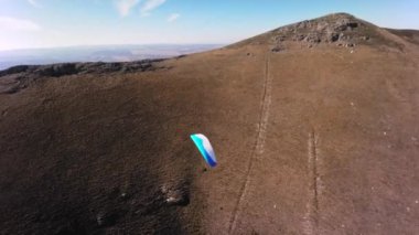 Paraşütçü bir sporcu, güneşli bir sonbahar gününde bir köyün yakınındaki küçük bir dağın yamacında yamaç paraşütü üzerinde uçar. FPV İHA kuadkopteri ile akro modda hava görüntüleme çekimi.
