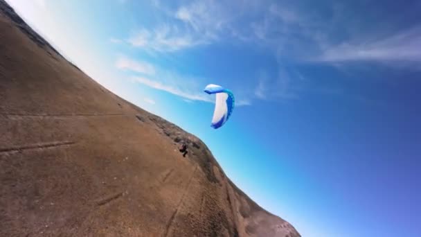 在一个阳光明媚的秋日 一位滑翔伞运动员驾驶着滑翔伞在一个村庄附近的一座小山的斜坡上飞行 用Fpv无人驾驶四联直升机在直升机模式下的空中拍摄 — 图库视频影像