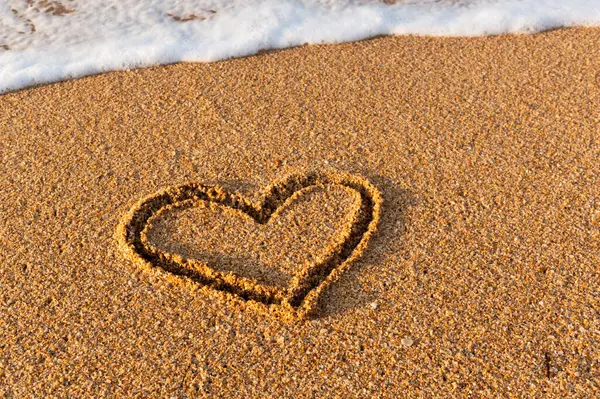 A heart is drawn on the sand on the beach during the day. Heart shape. Heart symbol. Love. Sea foam.