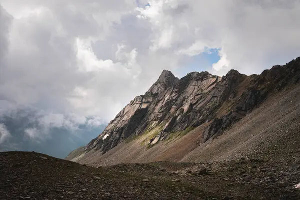 Close-up of a mountain wall at daytime against the backdrop of cumulus clouds.