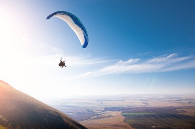 Mavi gökyüzünde bulutların ve mavi gökyüzünün arka planında bir paraglider uçuyor. Güneşli bir günde gökyüzünde paraşütle atlamak