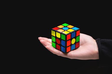 Rubiks küpü tutan kadın elleri. Siyah arka plandaki avuç içi, beynin ve motor becerilerin gelişimi için bir oyuncak getiriyor..