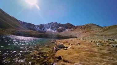 Sonbaharda bir dağ gölü kuş bakışı, dağ manzarası. Kızıl kaya ve yeşil göl, su ve kıyı şeridi üzerinde hızlı bir üstgeçit..