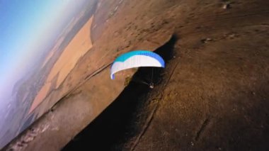 Bir FPV insansız hava aracının hava görüntüsü. Bir paraglider atleti küçük bir dağın yamaçlarına yakın uçar. Sonbaharda FPV insansız hava aracından kırsal alanlarda ücretsiz paraşüt uçuşu.