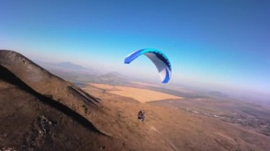 Bir FPV insansız hava aracının hava görüntüsü. Bir paraglider atleti küçük bir dağın yamaçlarına yakın uçar. Sonbaharda FPV insansız hava aracından kırsal alanlarda ücretsiz paraşüt uçuşu.