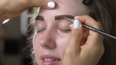 Kaş boyama. Bir fırçayla kaş boyası süren bir ustanın yakın çekimi. Kozmetik ameliyatlar, kalıcı kaş makyajı. Güzellik salonunda kaşların düzeltilmesi ve modellenmesi. Mükemmel kaşlar..
