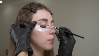 Kirpik kaplama ve boyama için modern spa kozmetik prosedürlerine yakın çekim. Genç bir kızın kadın yüzü ve profesyonel bir kozmetikçinin ellerine ait 4K 'lık bir video izlemek. güzellik ve sağlık.