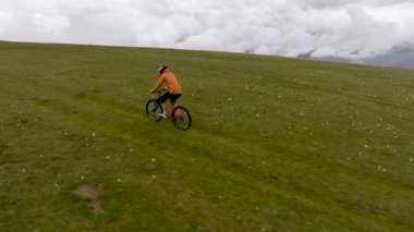 Korumalı bir kaskla dağ bisikleti süren bir bisikletçi dağların yüksek tepelerinde, bulutların ve dağların arkasında bisiklet sürüyor. hava görünümü.