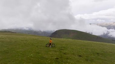 Korumalı bir kaskla dağ bisikleti süren bir bisikletçi dağların yüksek tepelerinde, bulutların ve dağların arkasında bisiklet sürüyor. hava görünümü.