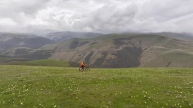 Drone, dik otlak bir tepede MTB bisikleti süren atletik bir adam boyunca uçuyor. Dağların güzel manzarası.