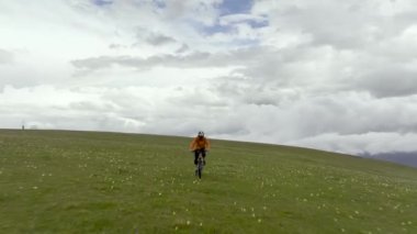 Korumalı bir kaskla dağ bisikleti süren bir bisikletçi dağların yüksek tepelerinde, bulutların ve dağların arkasında bisiklet sürüyor. hava görünümü.