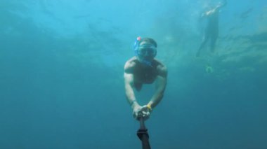Suyun altında yüzen bir adamın solunum tüpüyle maske takıp güneşli bir günde güneşlenirken selfie çektiği bir fotoğraf..