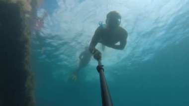 Sualtında maske takan, su altında yüzen ve gün boyunca deniz tabanında özçekim yapan, alglerle kaplı batık bir gemide yüzen bir adamın fotoğrafı..