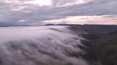 Yüksek açılı drone görüntüsü, yağmur mevsiminde dağların üzerindeki sis bulutları, doğanın video sahnesini yaratmak için güzel gün doğumu bulutları. 4K, bulutların bir nehir gibi hızlı aktığı dağlarda sisli günbatımı