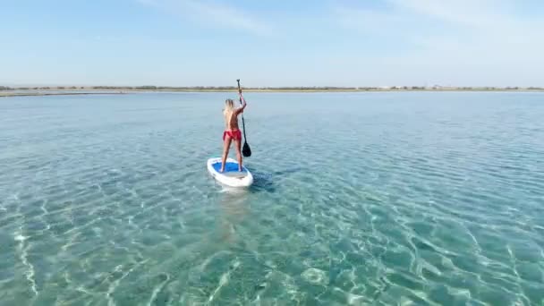 海上阳光明媚的一天 一个站在船桨上的年轻的高加索女人坐着她的蓝宝石板在空中旅行 — 图库视频影像