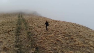 Turist gezgin adam, sisli ve alçak bulutlu bir dronla birlikte derin bir uçurumun yanındaki platoda yürüyor. Kuş gözü. hava görünümü.