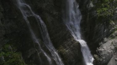 Güneşli bir günde dağların yükseklerinde bir buzul şelalesinin havadan görünüşü. 4k yüksekliğinde bir şelaleye yaklaş.