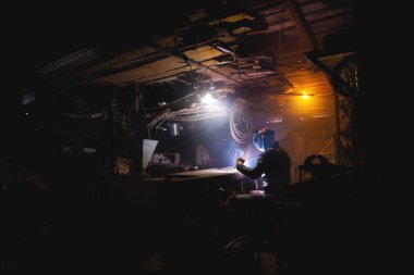 Elektrikli kaynak makinesiyle çalışan bir adam. Güvenlik gözlüklü ve deri ceketli bir adam garajında yedek parça pişiriyor..