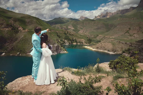 Love, wedding and married couple kissing by the lake outdoors in honor of their romantic marriage. Water, summer, mountains or a kiss.