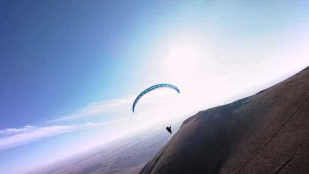 在一个阳光明媚的秋日 一位滑翔伞运动员驾驶着滑翔伞在一个村庄附近的一座小山的斜坡上飞行 用Fpv无人驾驶四联直升机在直升机模式下的空中拍摄 — 图库视频影像