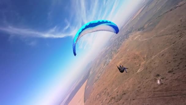 スポーツFpvドローンからの空中視界 パラグライダーのアスリートは小さな山の斜面の近くで飛ぶ Fpvドローンからの秋のビデオで田舎のフィールド上の無料パラグライダーフライト — ストック動画