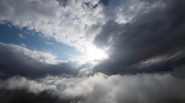 Hava görüntüsü. Gökyüzü kadar güzel, güneşli, bulutlu bir arazide uçuyor. Gökyüzünde yavaşça hareket eden tüylü beyaz bulutların ve bulutların üzerinde güzel ışınlarla parlayan güneşin inanılmaz videosu.