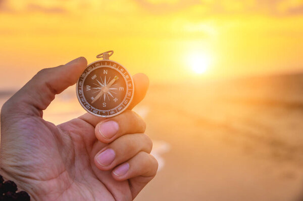Close-up of a mans hand holding a magnetic compass against the background of the setting sun and sea