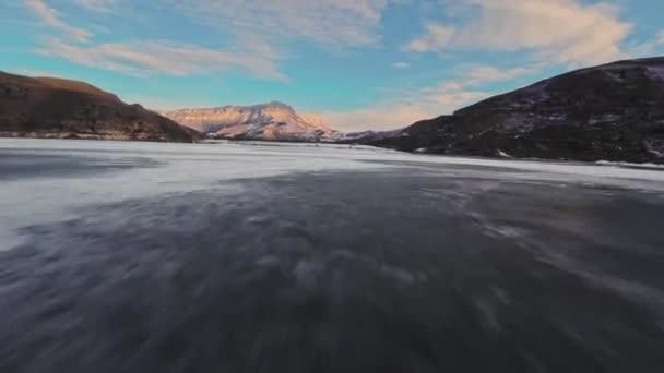 雪に覆われた日没の山を背景に凍った湖を飛行する迅速なFpvドローン飛行 — ストック動画