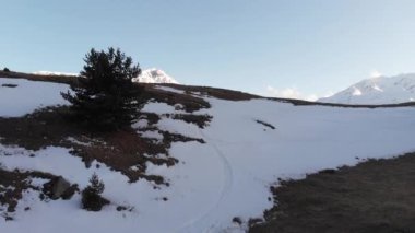 Ufuk çizgisinin üzerinde uçan insansız hava aracı arka planda karla kaplı dağlar ve gökyüzü olan bir vadi var..