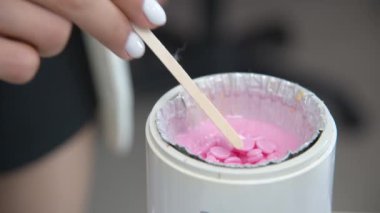 Sıcak pembe balmumu ve ahşap bir spatulayla balmumu ısıtıcısına yakın çekim. Tüy dökümü için sıcak mum. Güzellik salonu ekipmanları.