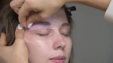 Kaş şeklinin düzeltilmesi ve yakın plan sıcak balmumu. Bir kaş sanatçısı bir kadının yüzüne balmumu sürer ve sertleştirilmiş pembe balmumunu çıkarır. Kaş şeklinin balmumu düzeltmesi.