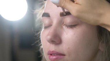 Kirpik kaplama ve boyama için modern spa kozmetik prosedürlerine yakın çekim. Genç bir kızın kadın yüzü ve profesyonel bir kozmetikçinin ellerine ait 4K 'lık bir video izlemek. güzellik ve sağlık.