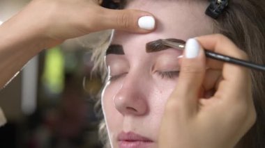 Güzellik salonunda kadın kaşlarının kalıcı renklendirilmesi için profesyonel prosedürler. Kaş boyama. Müşterilerin yüzlerini ve çalışan stilistleri yakından çek. 4K biçiminde sinematik görüntüler