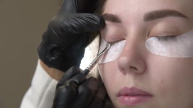 Kirpik kaplama ve boyama için modern spa kozmetik prosedürlerine yakın çekim. Genç bir kızın kadın yüzü ve profesyonel bir kozmetikçinin ellerine ait 4K 'lık bir video izlemek. güzellik ve sağlık.