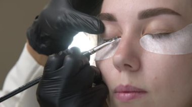 Kirpik kaplama ve boyama için modern spa kozmetik prosedürlerine yakın çekim. Genç bir kızın kadın yüzü ve profesyonel bir kozmetikçinin ellerine ait 4K 'lık bir video izlemek. güzellik ve sağlık.